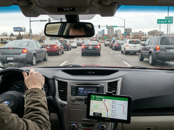 Commuter in car during morning rush on Eagle Road showing realistic commute scenario. Navigation displays actual times. Windshield view shows Treasure Valley destinations—downtown Boise, Micron, Meridian. Dashboard clock shows timing. Traffic patterns and drive time reality evident. Prepared, realistic expression versus surprise. Treasure Valley infrastructure and traffic visible through commuter perspective.